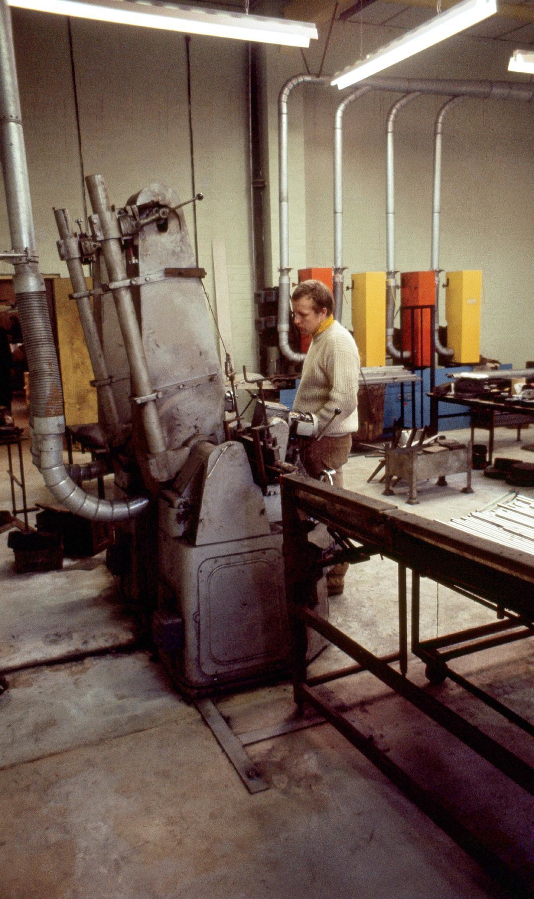   站在工厂车间里的Stuart Brisley、艺术家在被安置在Hille家具公司时彩涂的抛光机（背景与右侧），英国，1970