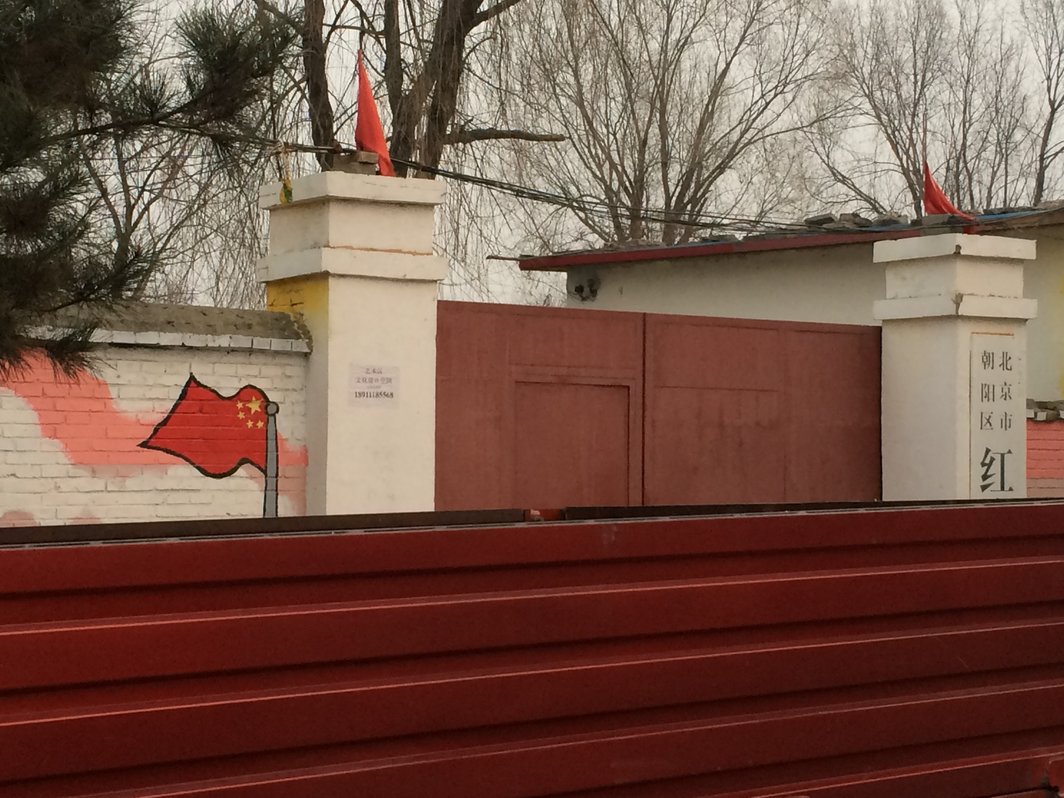 黑桥唯一的民工子弟红旗小学被红货车遮住，只露出真的红旗和绘制的红旗和黑体红字.