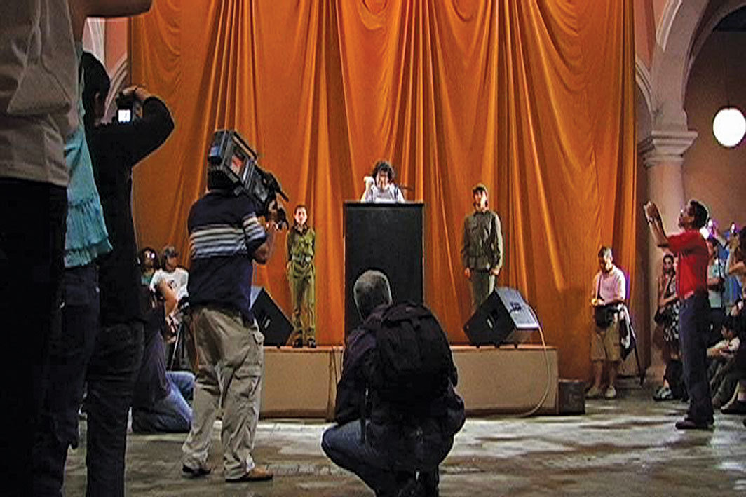 塔尼亚·布鲁古拉，《塔特林的私语 #6 [哈瓦那版]》，2009，舞台、讲台、麦克风，楼内外安装的扩音器，两名身着军服的工作人员，白鸽，每人一分钟不受审查的自由演讲，两百个带闪光一次性相机；表演现场，林飞龙当代艺术中心，哈瓦那，2009年3月29日；第十届哈瓦那双年展.