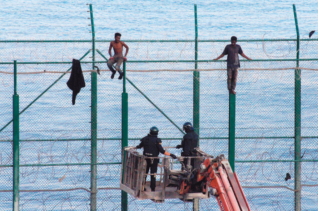 2019年8月30日，西班牙休达市（Ceuta），警察在接近边界围栏上的移民. 摄影：eduan Dris Regragui/EPA-EFE/Shutterstock.