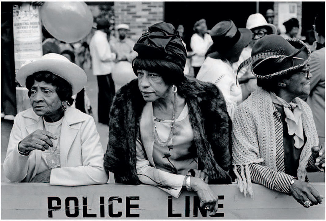 达伍德·贝，《游行中的三个女人，哈莱姆区，纽约》（Three Women at a Parade, Harlem, NY），1978，黑白银盐照片，8 1⁄8 × 11 7⁄8". 来自“美国哈莱姆区”系列，1975-79.