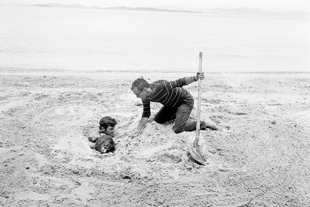 让-吕克·戈达尔在《狂人皮埃罗》片场，与让-保罗·贝尔蒙多（Jean-Paul Belmondo）和安娜·卡里娜（Anna Karina），法国波克罗勒岛（Porquerolles Island），1965. 图片：Alain Nogues/Getty Images.