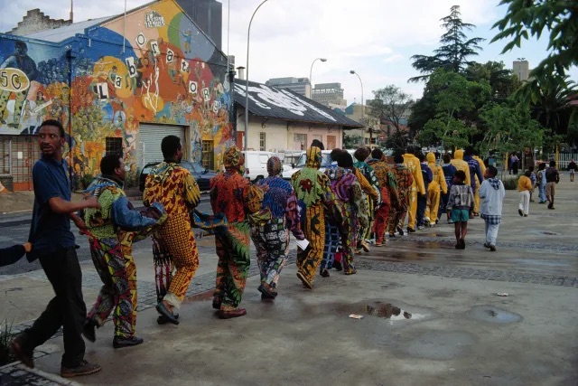 露西与豪尔赫·奥尔塔（Lucy and Jorge Orta），《纽带建筑》，1997，十六套由荷兰蜡染印花棉布、坎加布和拉链制成的服装. 公共行动现场，约翰内斯堡，1997。出自第二届约翰内斯堡双年展. 图片提供：Lucy Orta. © Artists Rights Society (ARS), New York/ADAGP, Paris.